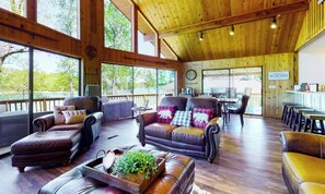 A spacious indoor area with leather sofas and a dining table, large windows offering views of the outdoors. - Norris Lake Cabin | Dock + Games (Jacksboro)