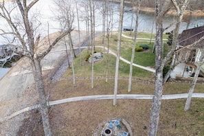 A residential area with a paved pathway, a small garden with trimmed bushes, and a body of water in the background. - Norris Lake Cabin | Dock + Games (Jacksboro)