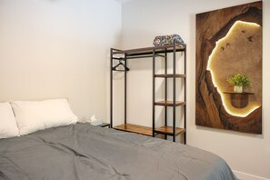 Une chambre avec un lit superposé, une table de chevet, une étagère murale agrémentée d’une plante et un grand tableau abstrait.
