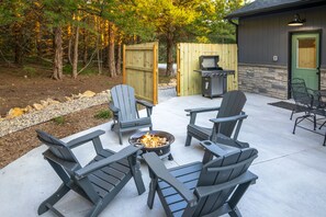 An outdoor patio with Adirondack chairs, a fire pit, and a grill area.