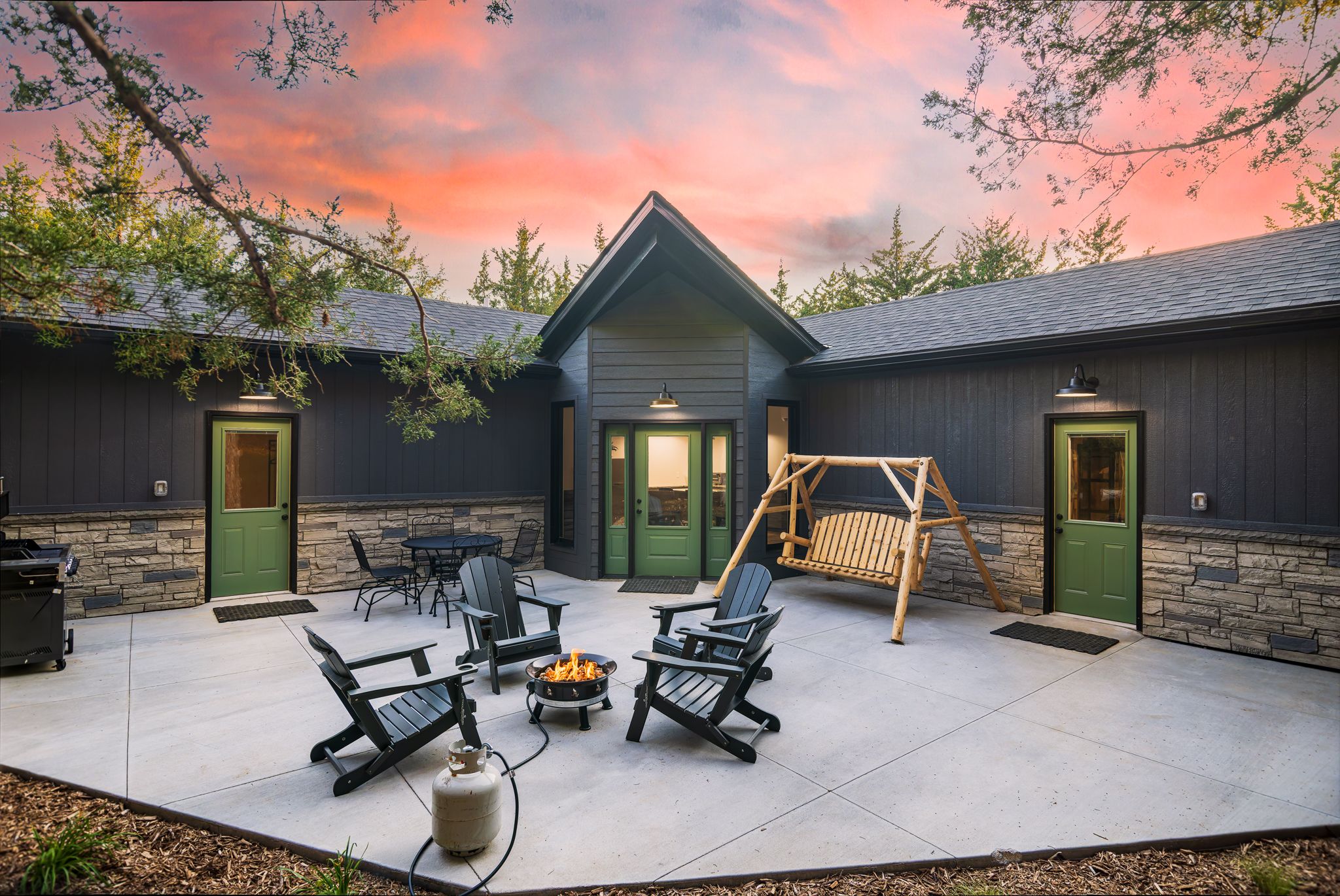 A covered outdoor patio with Adirondack chairs, a fire pit, and a wooden swing set.