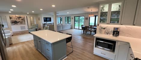 A spacious kitchen with a central island, a dining area with a table and chairs, and a living area with a sofa and television.