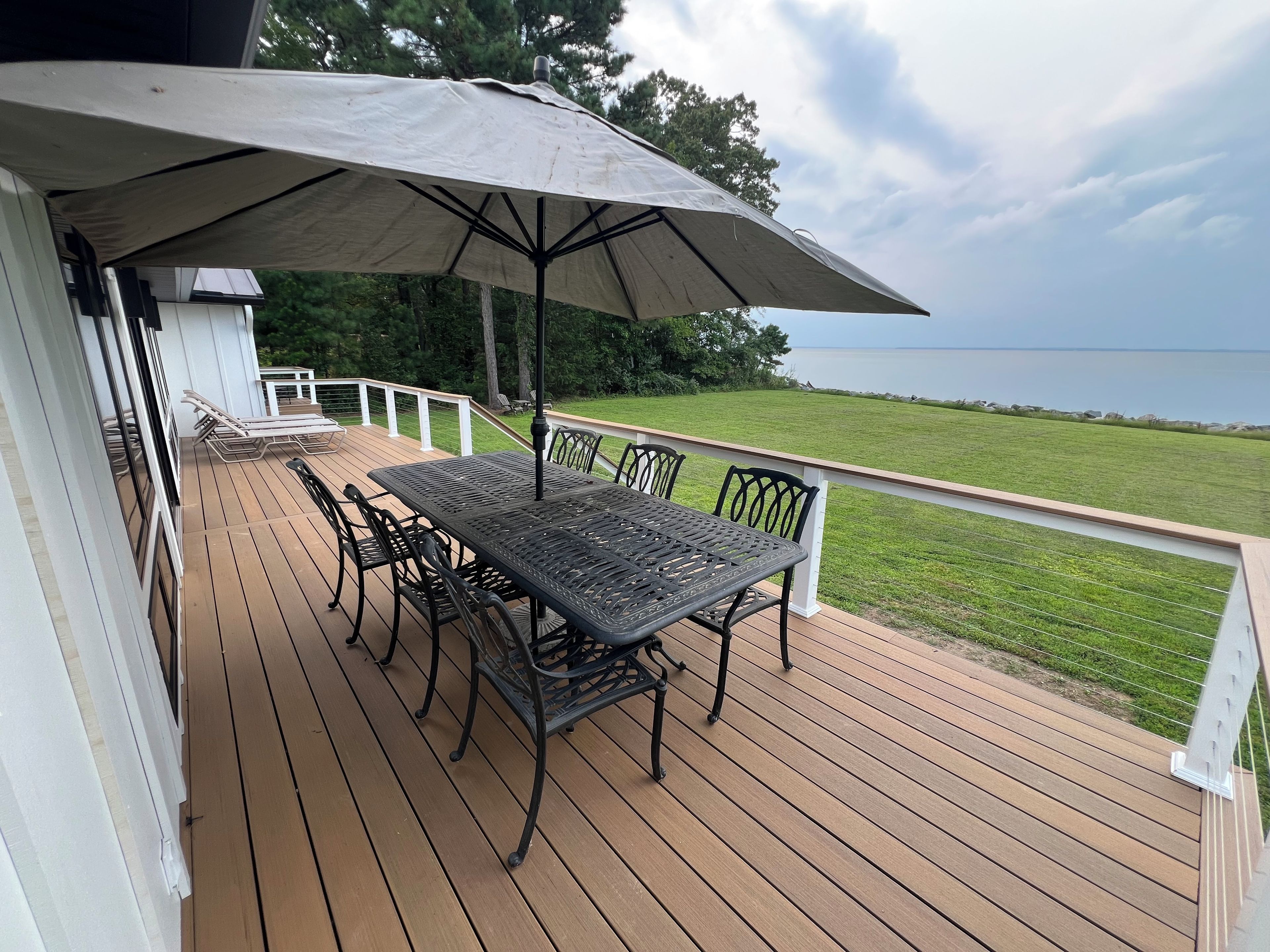 A wooden deck with a table and chairs, an umbrella, and a view of the water.