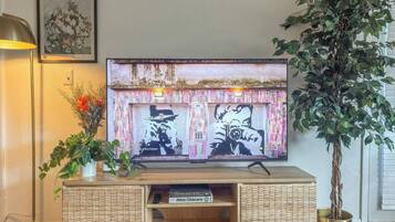 Ein Fernseher steht auf einer Holzkommode, daneben ein Zimmerpflanze.