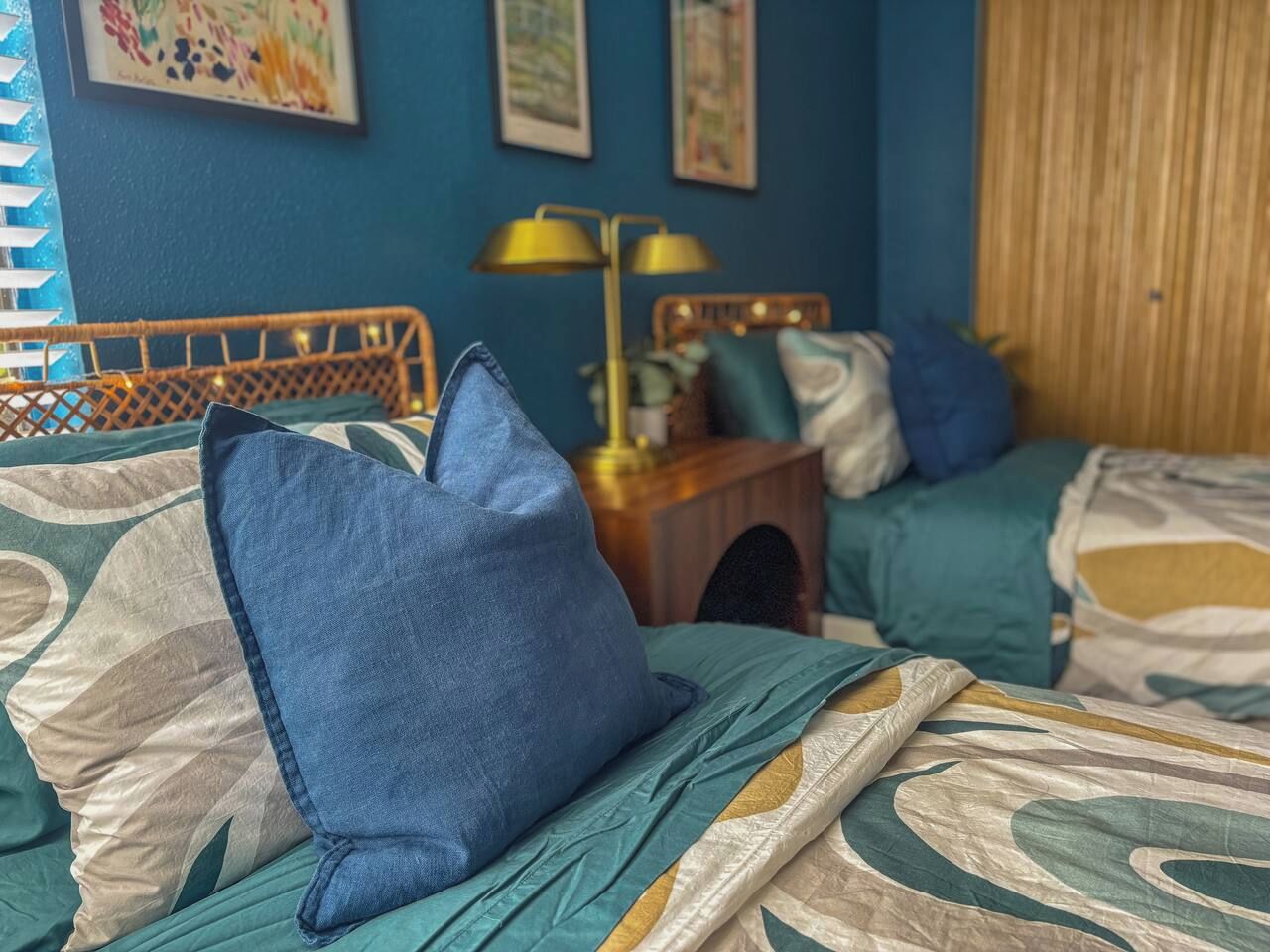 Une chambre avec deux lits, chacun agrémenté d’un oreiller bleu et d’une couvre-lit à motifs. On y trouve une table de chevet avec une lampe, ainsi qu’une petite table sur laquelle est posée une plante.