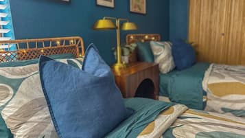 Une chambre avec deux lits, chacun agrémenté d’un oreiller bleu et d’une couvre-lit à motifs. On y trouve une table de chevet avec une lampe, ainsi qu’une petite table sur laquelle est posée une plante.