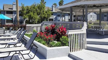 Un espace aménagé au bord de la piscine, avec des chaises longues, un coin salon abrité et un jardin agrémenté de fleurs rouges.