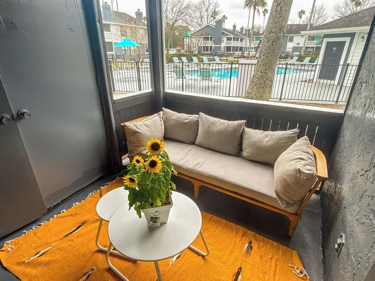 Ein Eckzimmer mit einer Couch, einem kleinen runden Tisch und einem Blumentopf mit Sonnenblumen.