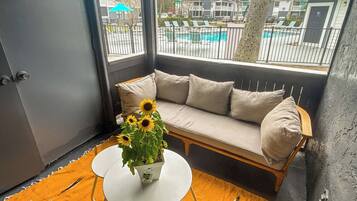 Ein Eckzimmer mit einer Couch, einem kleinen runden Tisch und einem Blumentopf mit Sonnenblumen.