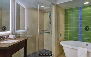 Un baño con ducha envuelta en vidrio, lavamanos con encimera de granito y bañera blanca.