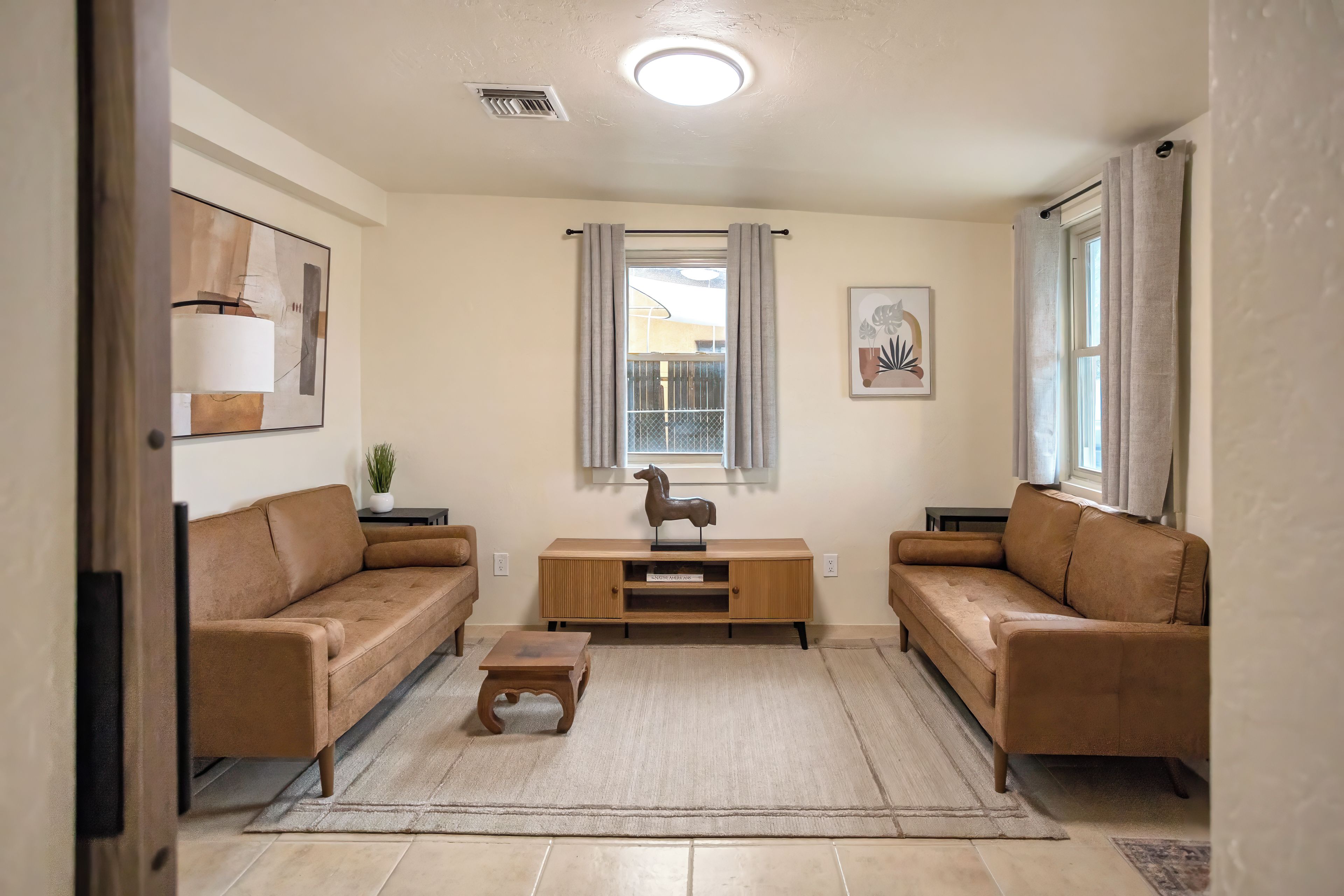 A living room with two brown sofas, a wooden coffee table, a small plant, and a window with curtains.