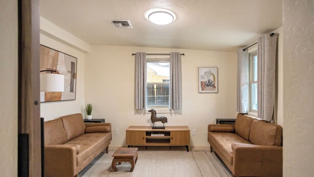 A living room with two brown sofas, a wooden coffee table, a small plant, and a window with curtains. - 1945 Adobe in the Heart of Tucson (Tucson)