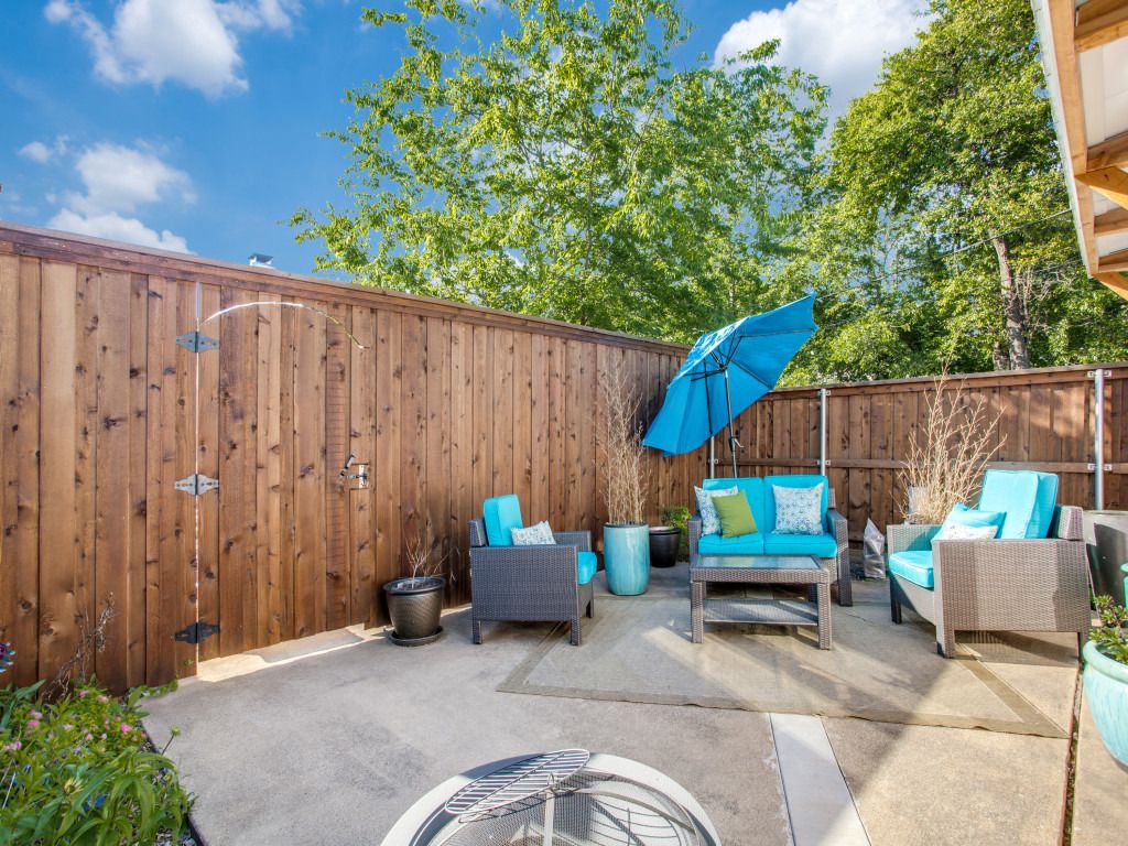 An outdoor patio area with a wooden fence, outdoor furniture, and a blue umbrella.