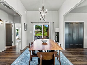 A dining area with a wooden table, chairs, a chandelier, and a view of the outdoors. - GJ Getaway - Fire Pit + Bocce + Private Yard! (Grand Junction)