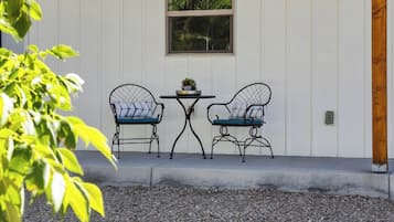Un espacio al aire libre con dos sillas y una mesa, rodeado de grava y una pared blanca con una ventana.