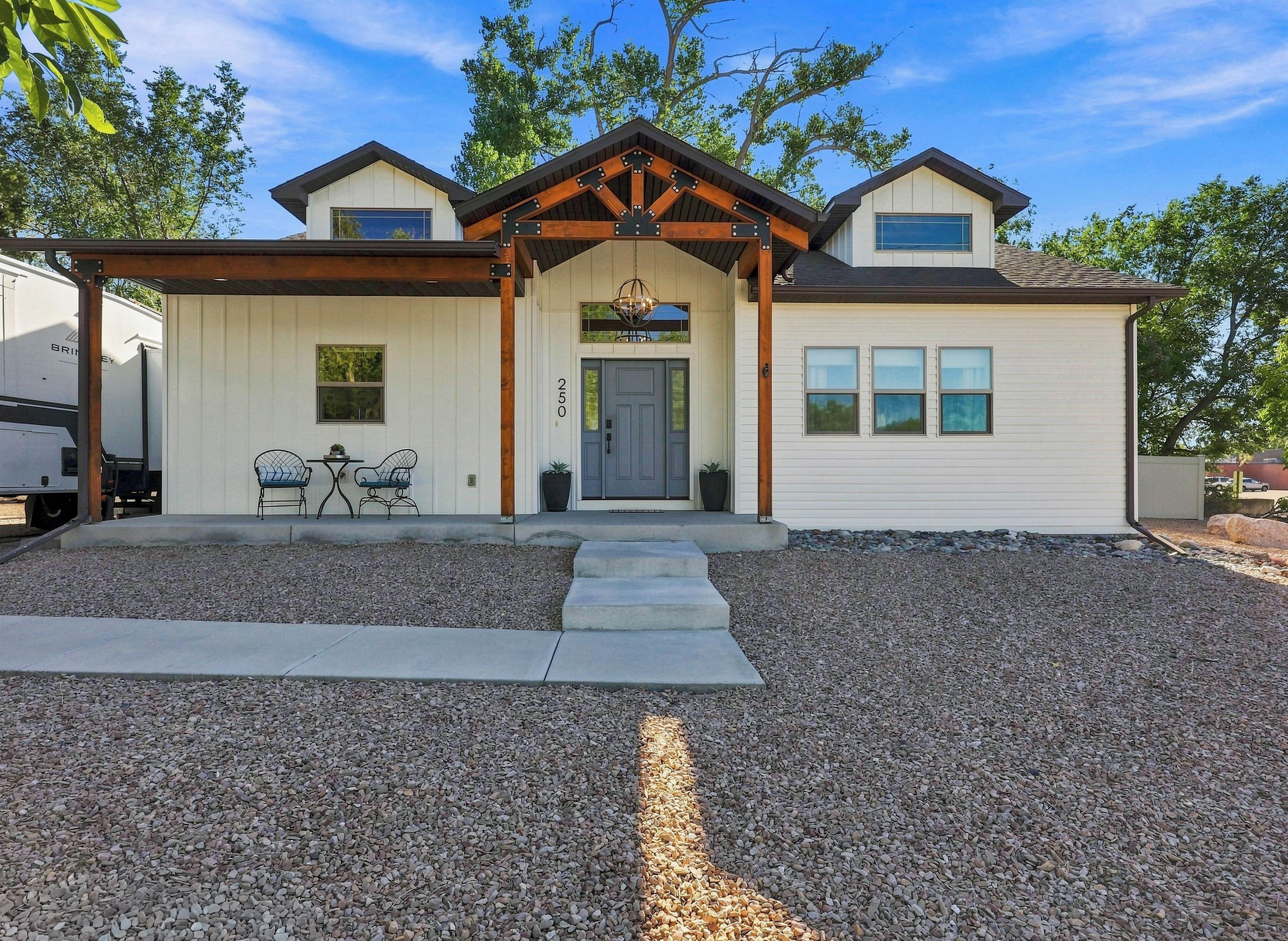 Una casa de dos pisos con un porche cubierto, una puerta principal y un pequeño patio con mobiliario exterior.