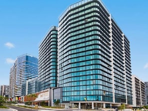 A modern high-rise building with multiple floors, large windows, and a curved facade. - High-Rise 2BR Retreat with Water Views (Wentworth Point)