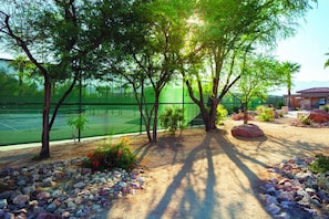 Una cancha de tenis con red, rodeada de árboles y rocas.