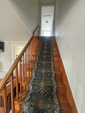 A staircase with a patterned carpet, wooden handrails, and a white door at the top. - 4BR Ski-Season Home: 8 Min to Okemo + Private Studio (Cavendish)