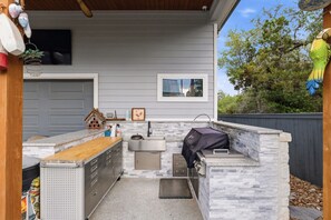 Une cuisine extérieure dotée d’un plan de travail en pierre, d’un barbecue et d’un évier.