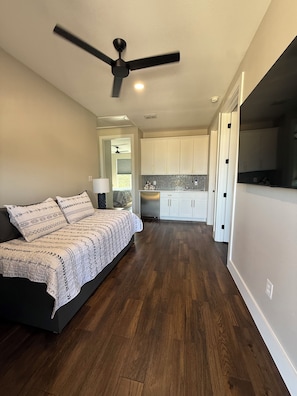 Une chambre avec un lit, un ventilateur de plafond et une vue sur un coin cuisine.
