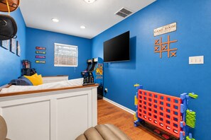 A room with a bed, a television mounted on the wall, a window with blinds, and a sign indicating it's the game room. - Austin Fun House Huge Private Yard, Pickleball, Cowboy Pool & Hot Tub (Austin)