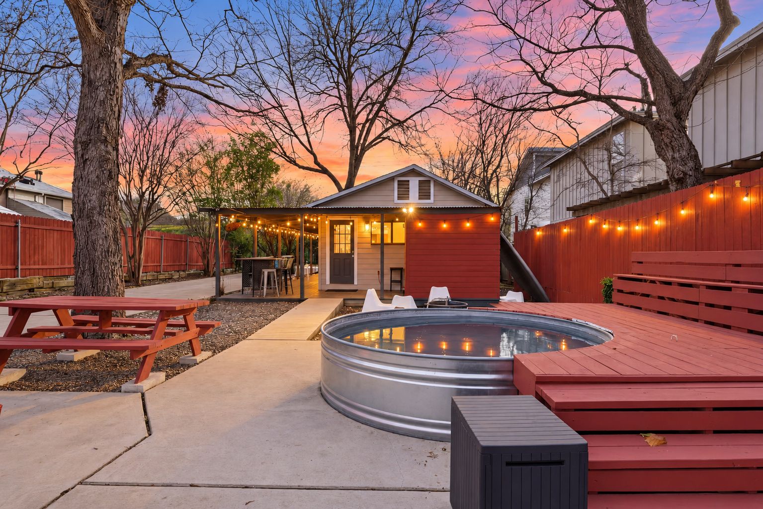 A backyard with a hot tub, picnic table, and string lights.
