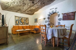 A cozy living room with a stone wall, a sofa, a dining table with chairs, and a painting. - Cozy Cave Home in Gran Canaria (Artenara)
