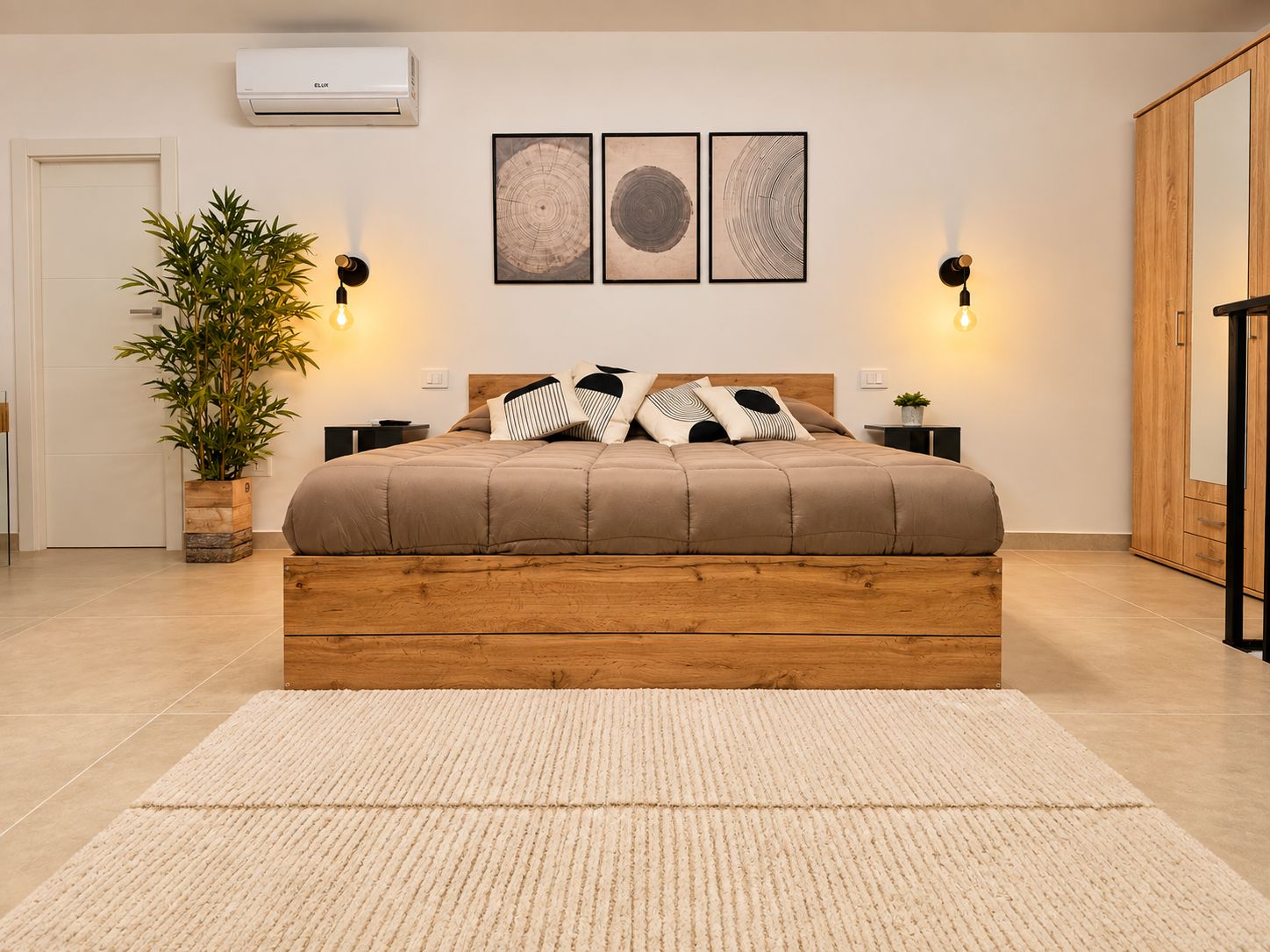 A bedroom with a wooden bed, two bedside lamps, a potted plant, and three framed artworks on the wall.
