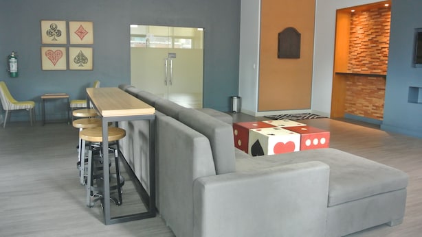 A modern lounge area with a grey sofa, wooden bar stools, and a wooden table. - One Uptown Residence BGC
Sky-High BGC Stay | Work & Relax (Makati City)