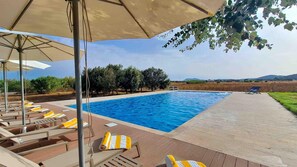 Una piscina amb gandules i ombrel·les, envoltada d'arbres i vista al paisatge.