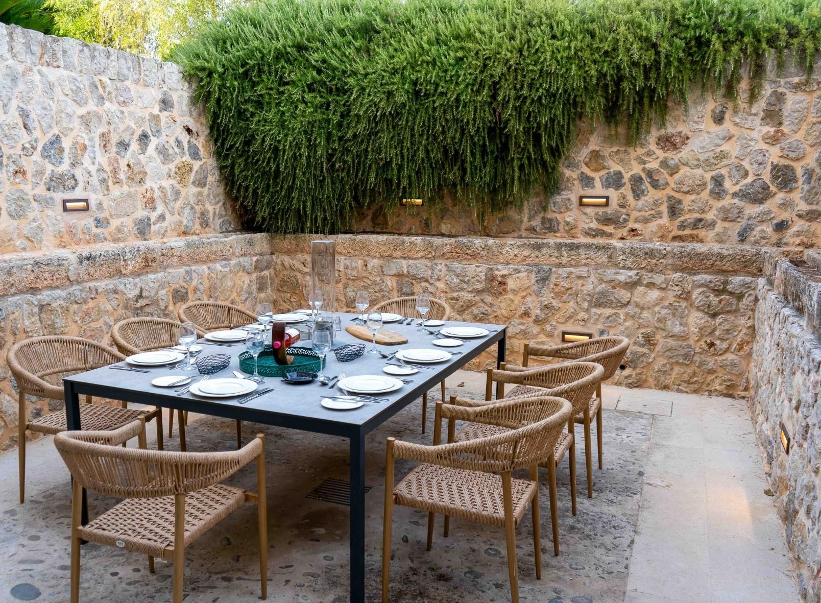 An outdoor dining area with a stone wall, a table set for six, and wicker chairs.