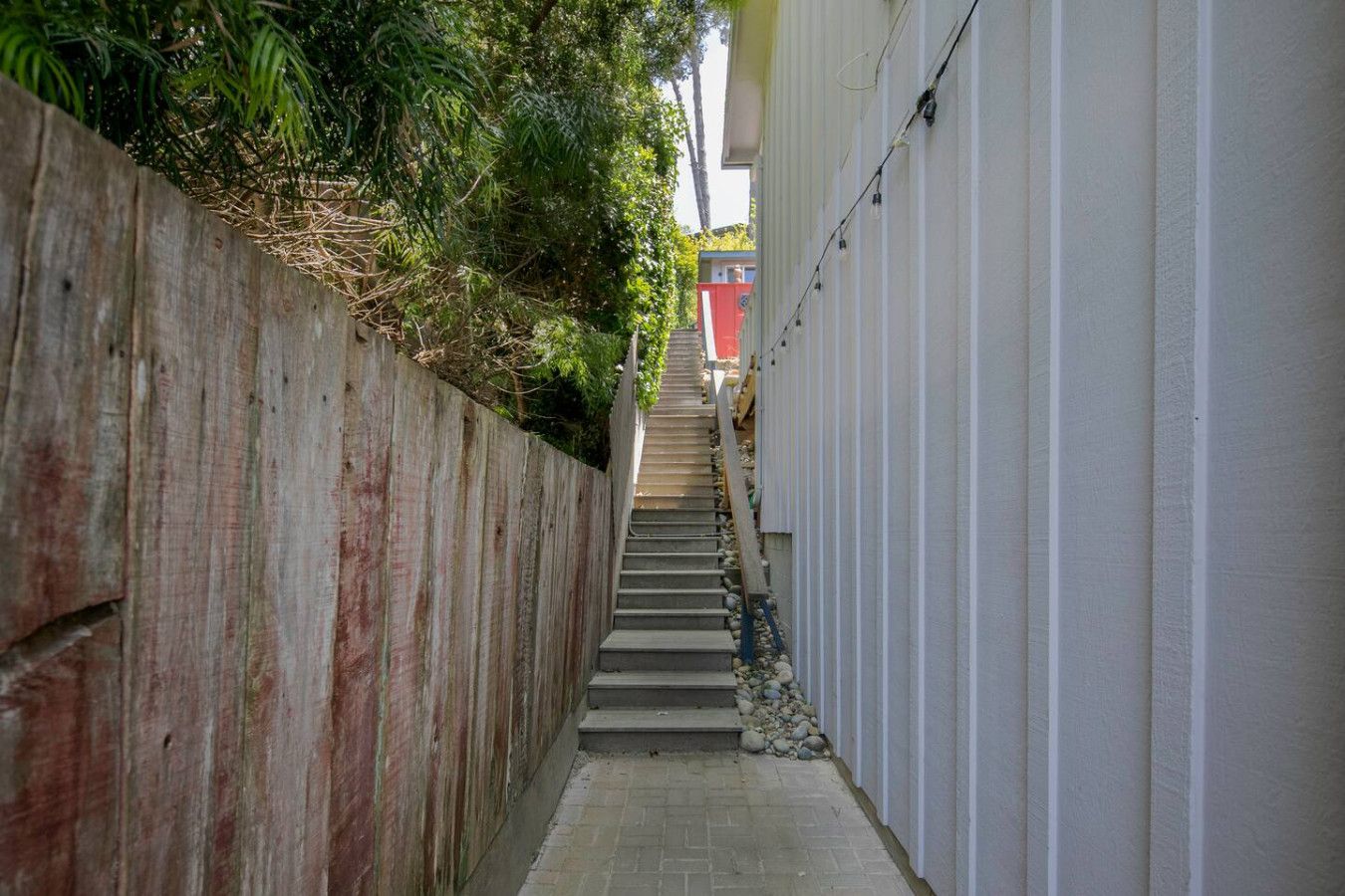 A narrow alleyway with a wooden fence on one side and a white wall on the other, leading to a staircase.