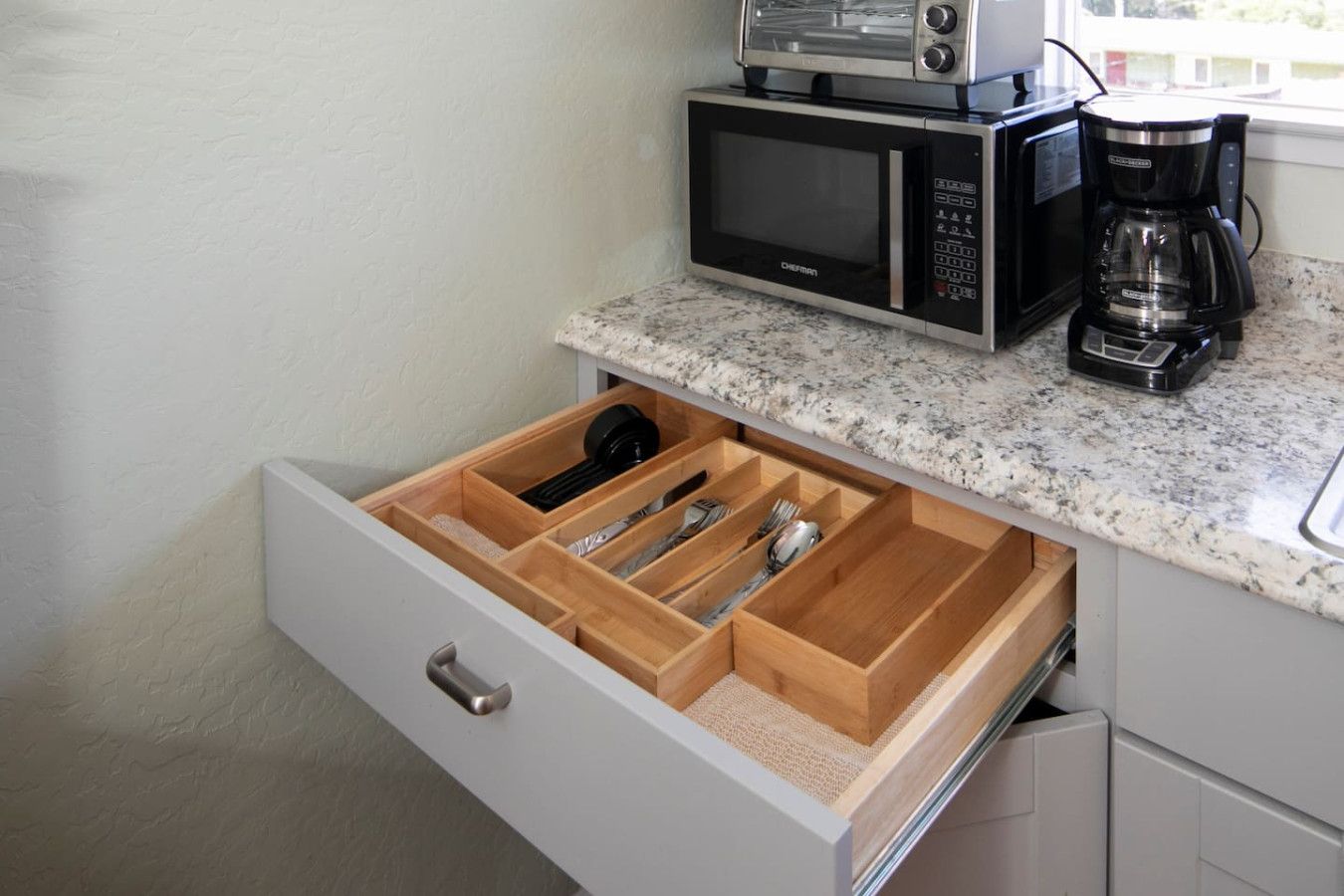 Una cocina con un organizador de cajones que contiene utensilios, un microondas y una cafetera.