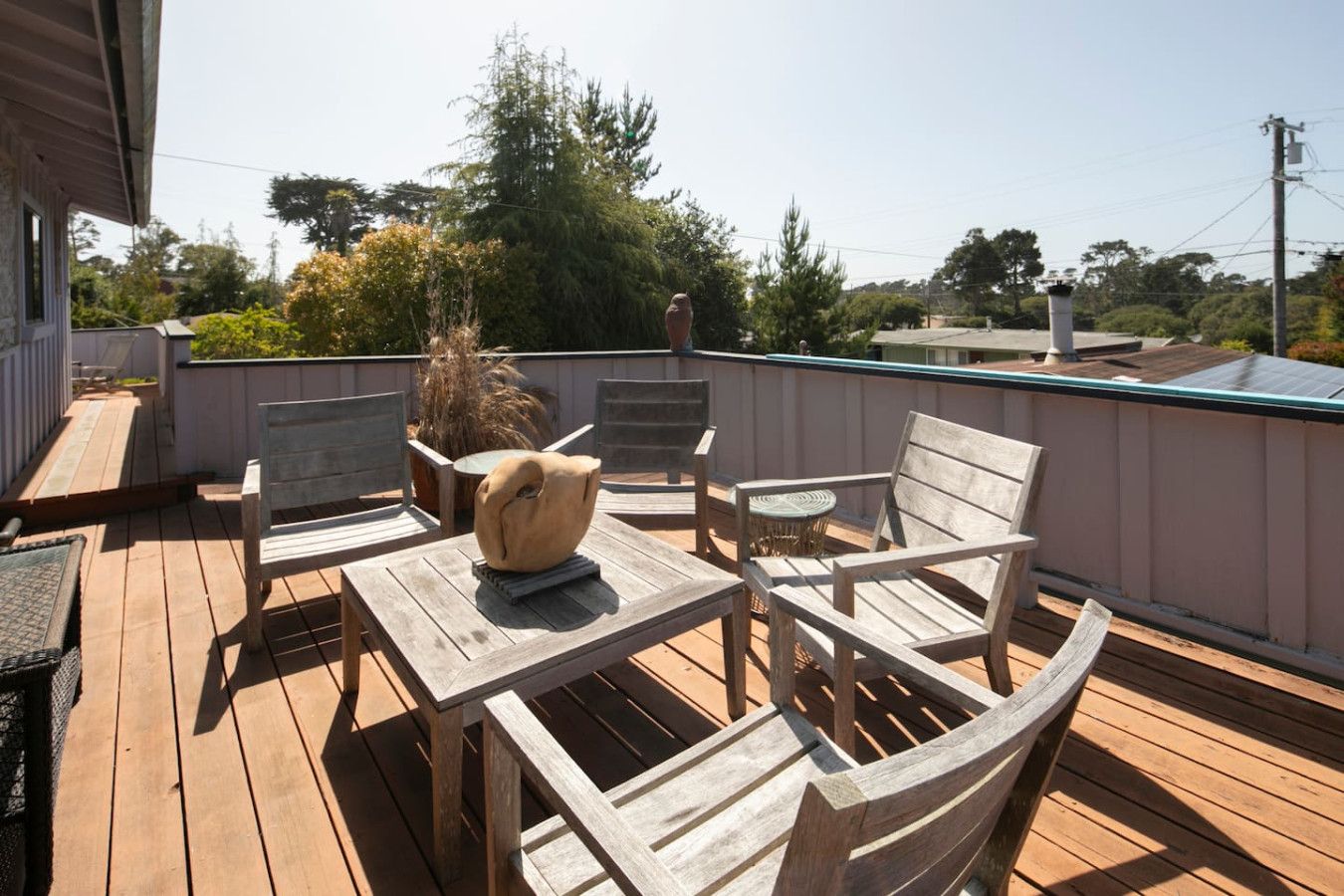 Une terrasse en bois aménagée avec du mobilier d’extérieur, notamment une table et des chaises, ainsi qu’un vase décoratif.