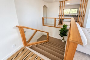 Eine Treppe mit hölzernen Geländern führt zu einem Bereich im zweiten Stock mit einer Küche und einer Pflanze.