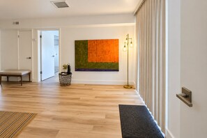 Ein modernes Interieur mit Holzboden, einer Bank, einem an der Wand hängenden abstrakten Gemälde, einer Stehlampe und einer Tür zu einem anderen Raum.