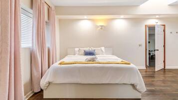 A bedroom with a large bed, a bedside table, a nightstand, and a door leading to another room.