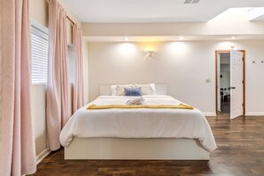 A bedroom with a large bed, a bedside table, a nightstand, and a door leading to another room. - Cozy Comfort - Steps to Cannery Row & Ocean (Pacific Grove)
