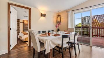 A dining area with a table set for four, a wooden floor, and a view through a glass door to an outdoor deck.