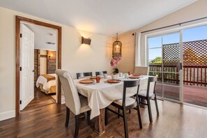 A dining area with a table set for four, a wooden floor, and a view through a glass door to an outdoor deck. - Cozy Comfort - Steps to Cannery Row & Ocean (Pacific Grove)
