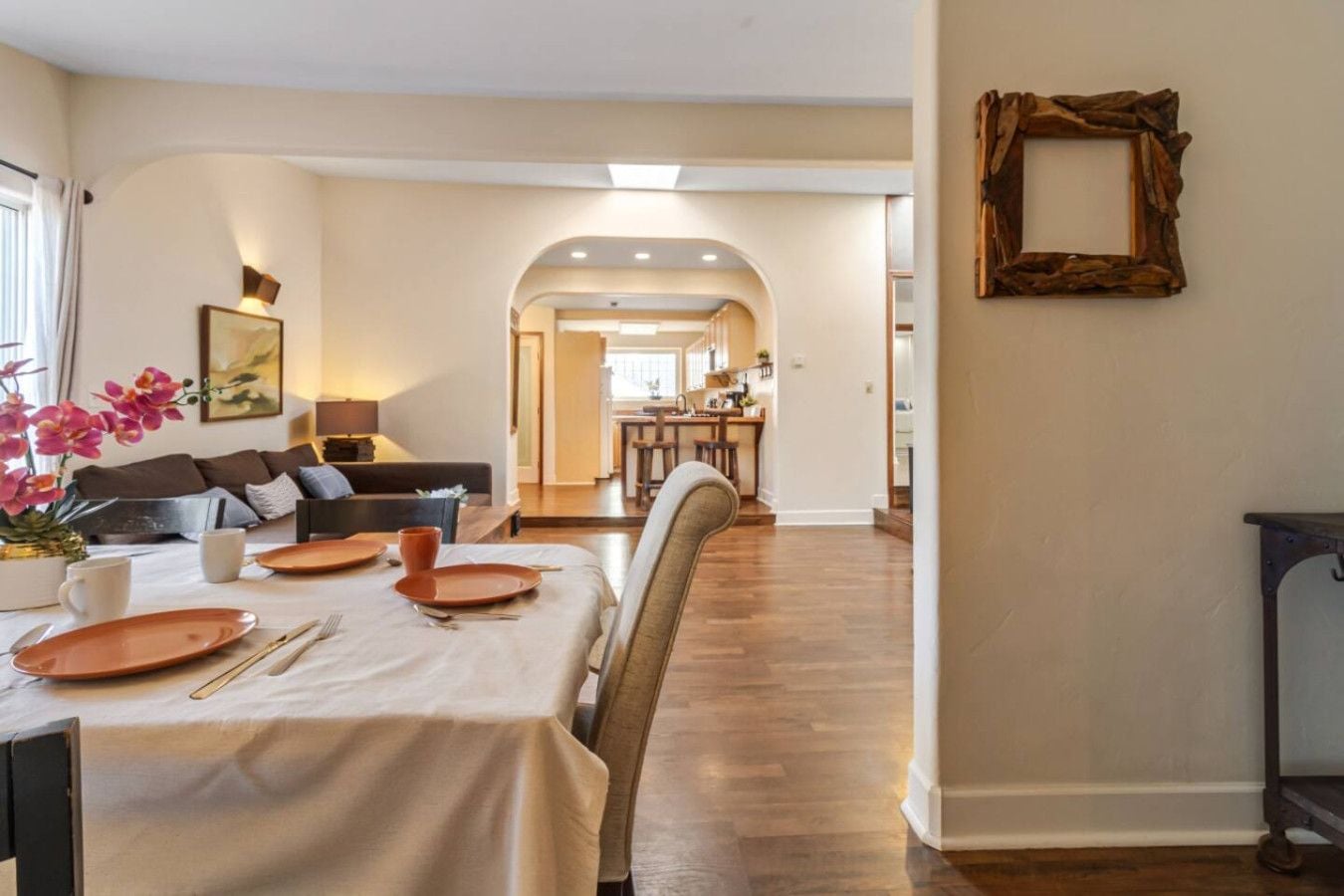 Un coin repas avec une table dressée pour deux personnes, un canapé et une cuisine en arrière-plan.