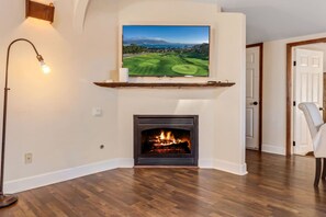 A living room with a fireplace, a mounted television, and a floor lamp. - Cozy Comfort - Steps to Cannery Row & Ocean (Pacific Grove)