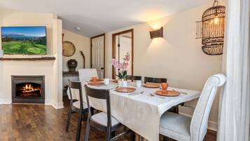 A dining area with a fireplace, a television mounted on the wall, and a chandelier.