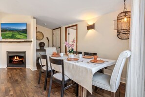 A dining area with a fireplace, a television mounted on the wall, and a chandelier. - Cozy Comfort - Steps to Cannery Row & Ocean (Pacific Grove)
