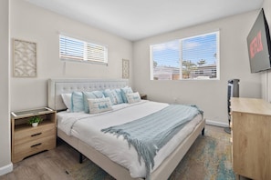 A bedroom with a bed, bedside tables, a TV, and a window. - Bay Park Retreat | 4BR Near Beaches (San Diego)