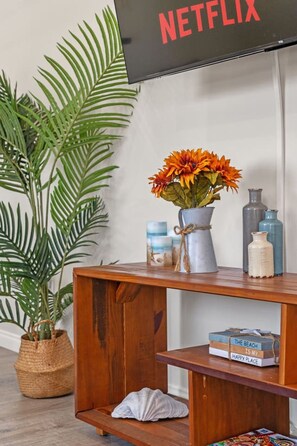 A living room with a wooden console table, a potted plant, decorative vases, and a television displaying the Netflix logo. - Bay Park Retreat | 4BR Near Beaches (San Diego)