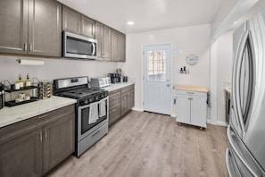 A modern kitchen with stainless steel appliances, wooden cabinets, and a white door. - Bay Park Retreat | 4BR Near Beaches (San Diego)