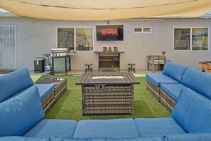 Un espace de vie extérieur accueillant, avec un foyer, des canapés bleus, un coin bar et un panneau Netflix.