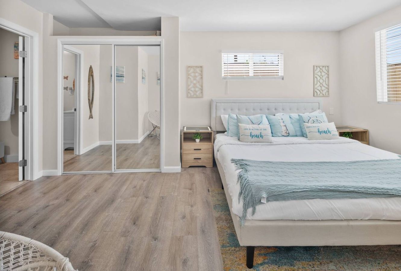 A bedroom with a large bed, a nightstand, a mirror, and a door leading to a bathroom.